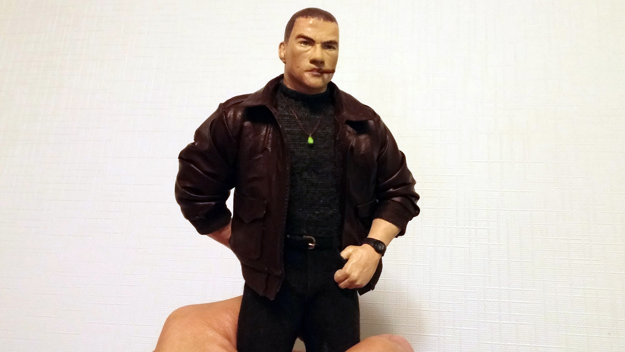 One image in a medium close up of the miniature statue fully clothed with cigar in mouth, jade necklace and sport watch on wrist